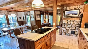 A kitchen with a central island, wooden cabinets, stone accents, and a dining area with chairs and a table. - Tall Pines Retreat, Somesville|Mt. Desert. 15 min to Bar Harbor, 5 to Acadia (Mt Desert)