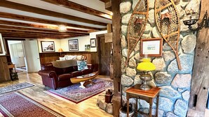 A cozy living room with a stone wall, wooden beams, a leather sofa, and a coffee table. - Tall Pines Retreat, Somesville|Mt. Desert. 15 min to Bar Harbor, 5 to Acadia (Mt Desert)