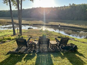 A lakeside seating area with Adirondack chairs and a picnic table, surrounded by rocks and grass.