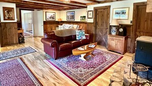 A cozy living room with a leather sofa, a coffee table, and a fireplace. There are wooden beams on the ceiling and a rustic wooden door. - Tall Pines Retreat, Somesville|Mt. Desert. 15 min to Bar Harbor, 5 to Acadia (Mt Desert)