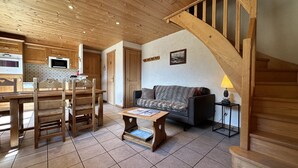 A cozy living room with a wooden staircase, a sofa, a coffee table, and a kitchen area with wooden cabinets and a tiled backsplash.