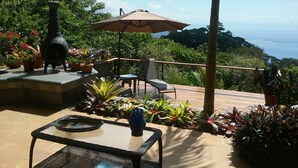 Eine Terrasse im Freien mit einem Steintisch, Stühlen, einer blauen Vase und einem großen Sonnenschirm.