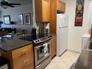 A kitchen with wooden cabinets, a stainless steel stove, a white refrigerator, and a granite countertop. - Our family Maui Condo..A home away from home. (Kihei)