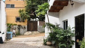 A courtyard with a gravel path, a wooden gate, and a building with a stone wall and a metal gate. - Casa Katrina #1 (Sayulita)