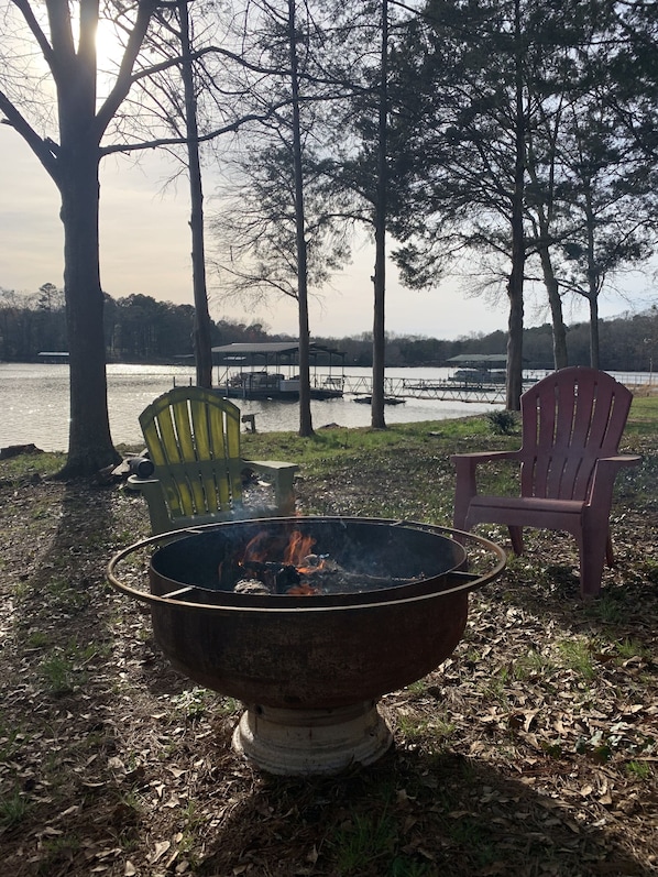 Relax by the fire pit in a serene lakeside setting, surrounded by Adirondack chairs.