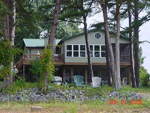 Situated in a wooded area, this cabin features a balcony and a front porch with Adirondack chairs.