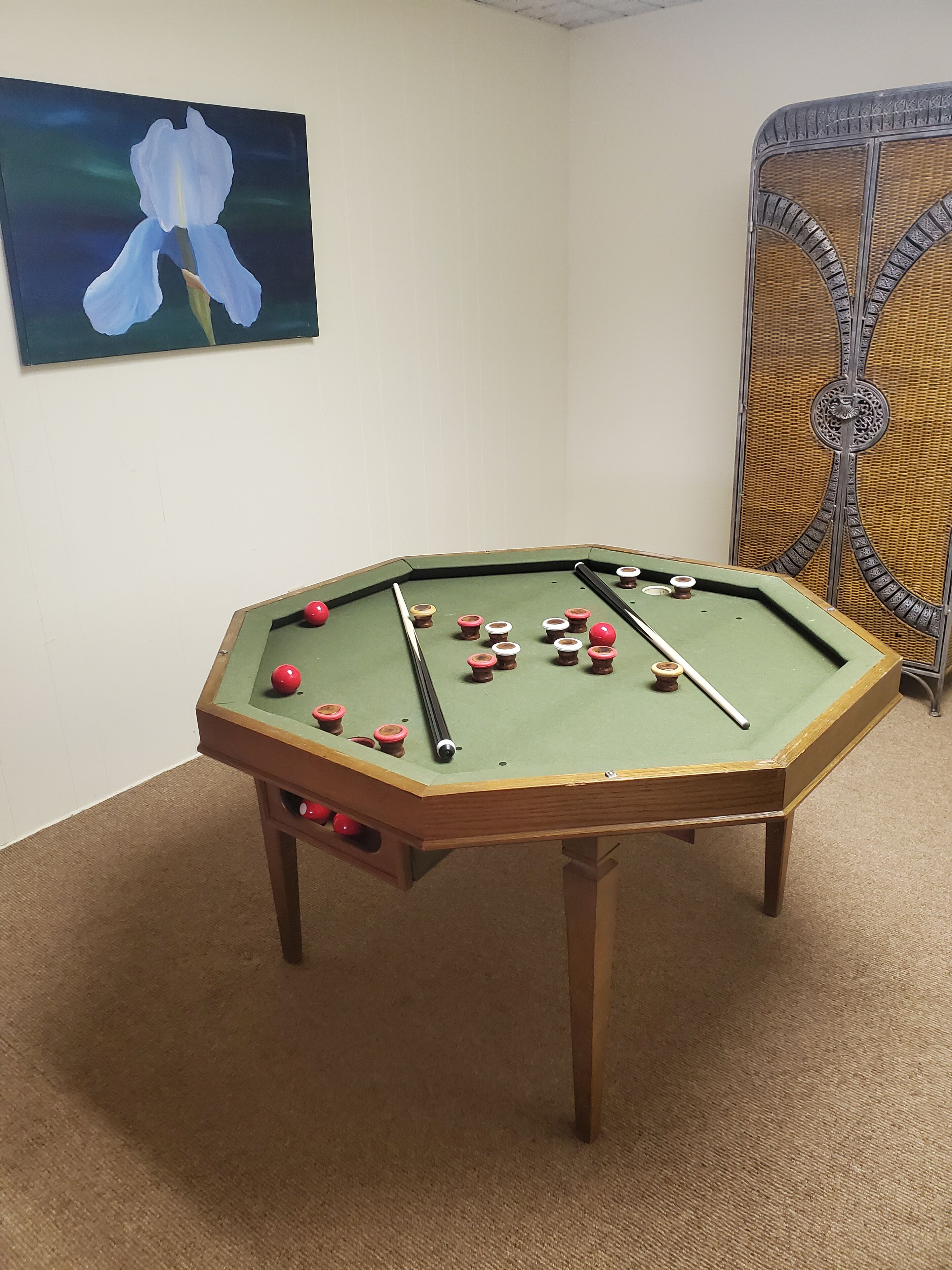 A pool table with balls and cues, a painting on the wall, and a decorative metal partition.