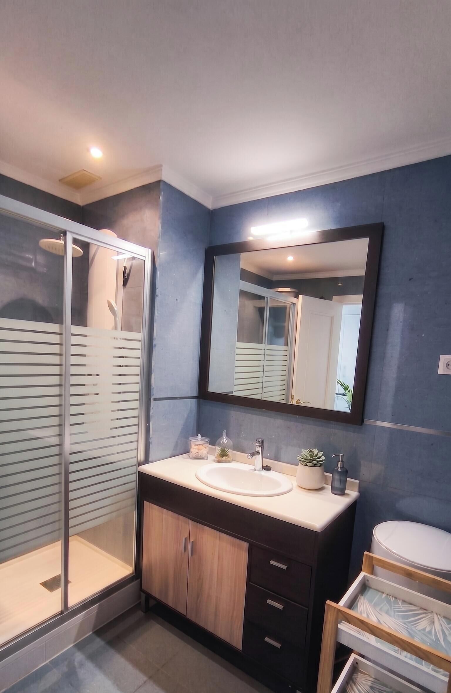 Une salle de bain moderne avec une douche à parois de verre, un grand miroir et un meuble-lavabo en bois.
