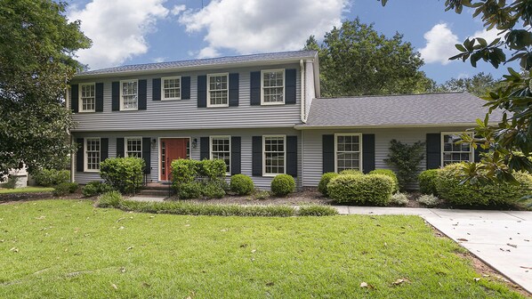A two-story house with a front porch, a red door, and a well-maintained lawn.