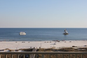 A beach with a boat and a sailboat in the water, and people on the sand.