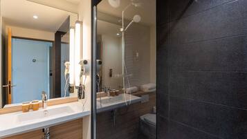 Une salle de bain moderne dotée d’une douche à parois de verre, d’un grand miroir et d’un meuble-lavabo avec un évier et un porte-serviettes.