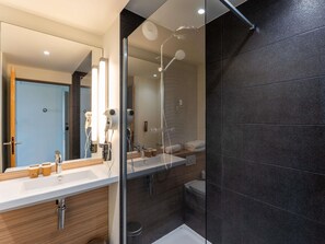 A modern bathroom with a glass-enclosed shower, a large mirror, and a vanity with a sink and towel rack.