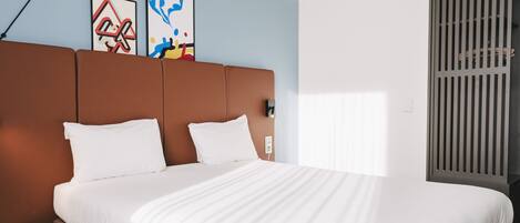 A modern hotel room with a large bed, a round side table, and two abstract paintings on the wall.