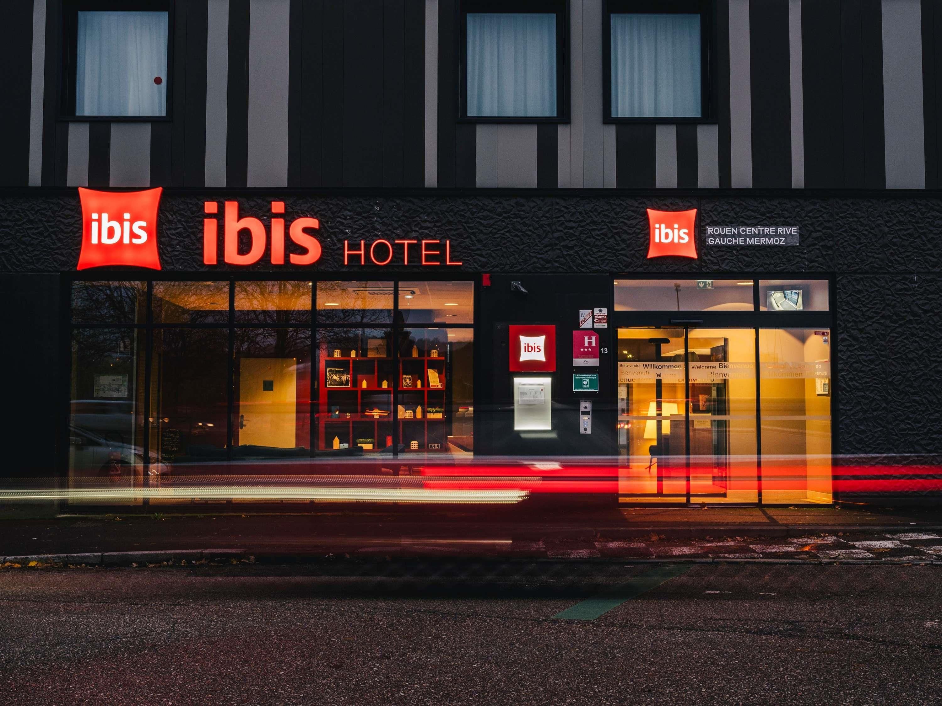 Das ibis Hotel mit moderner Fassade, großen Fenstern und einem markanten rot-weißen Logo.