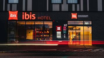 Das ibis Hotel mit moderner Fassade, großen Fenstern und einem markanten rot-weißen Logo.