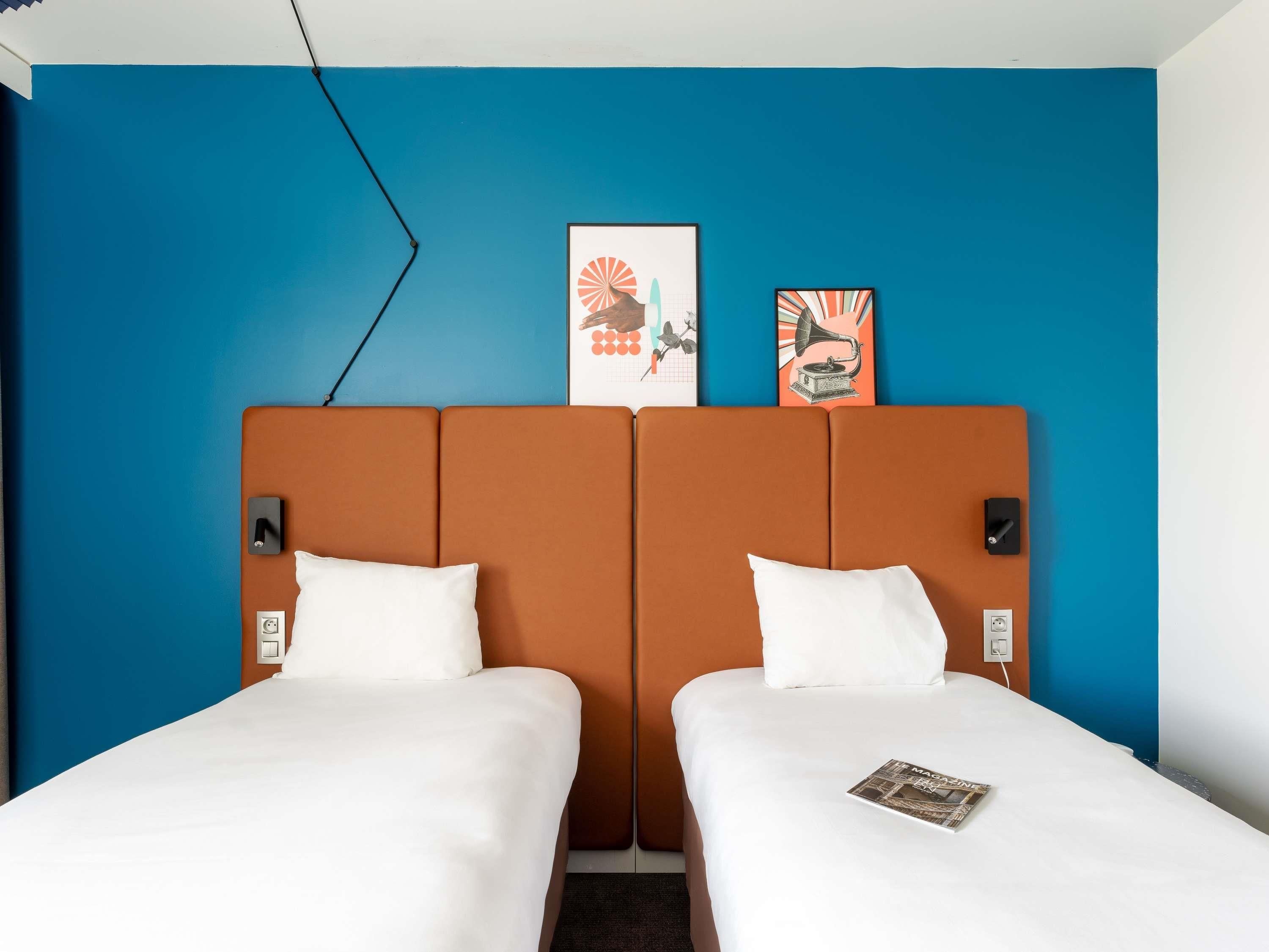 A hotel room with two beds, a blue accent wall, and artwork above the beds.