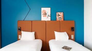 A hotel room with two beds, a blue accent wall, and artwork above the beds.