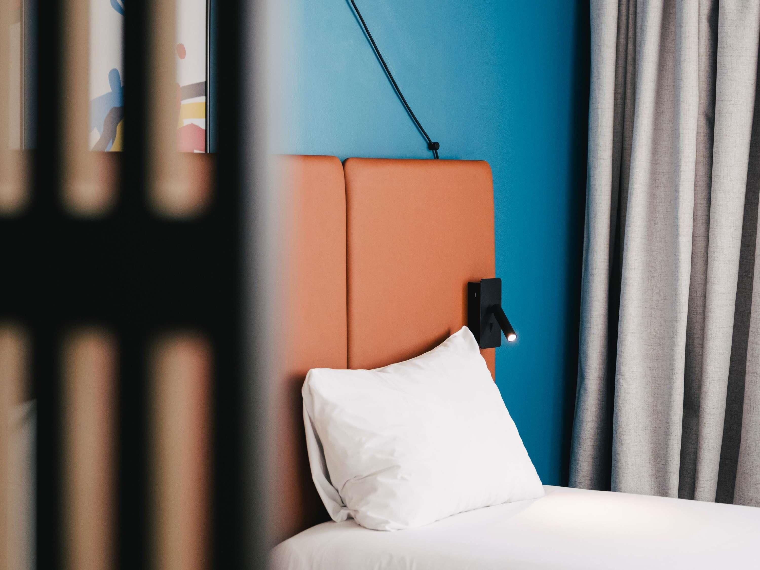 Ein Bett mit weißer Bettwäsche, einem Kopfteil und einer Wandleuchte.