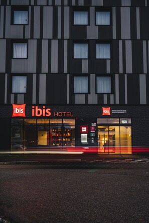 A modern hotel with a prominent "ibis" sign, large windows, and a well-lit entrance. - Ibis Rouen Centre Rive Gauche Mermoz (Rouen)