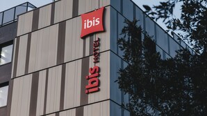 Um edifício moderno com um grande letreiro vermelho da Ibis, indicando que é um hotel.