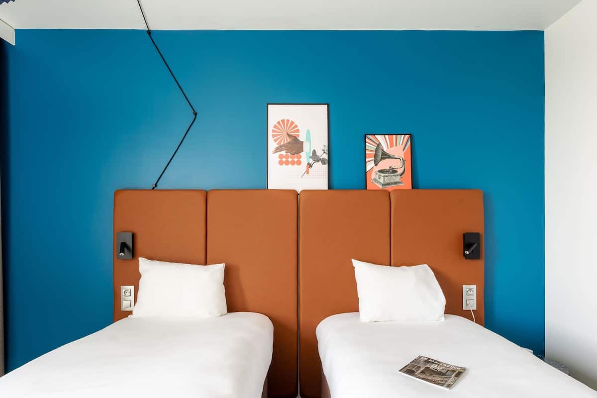 Ett hotellrum med två sängar, en blå accentvägg och konstverk ovanför sängarna.