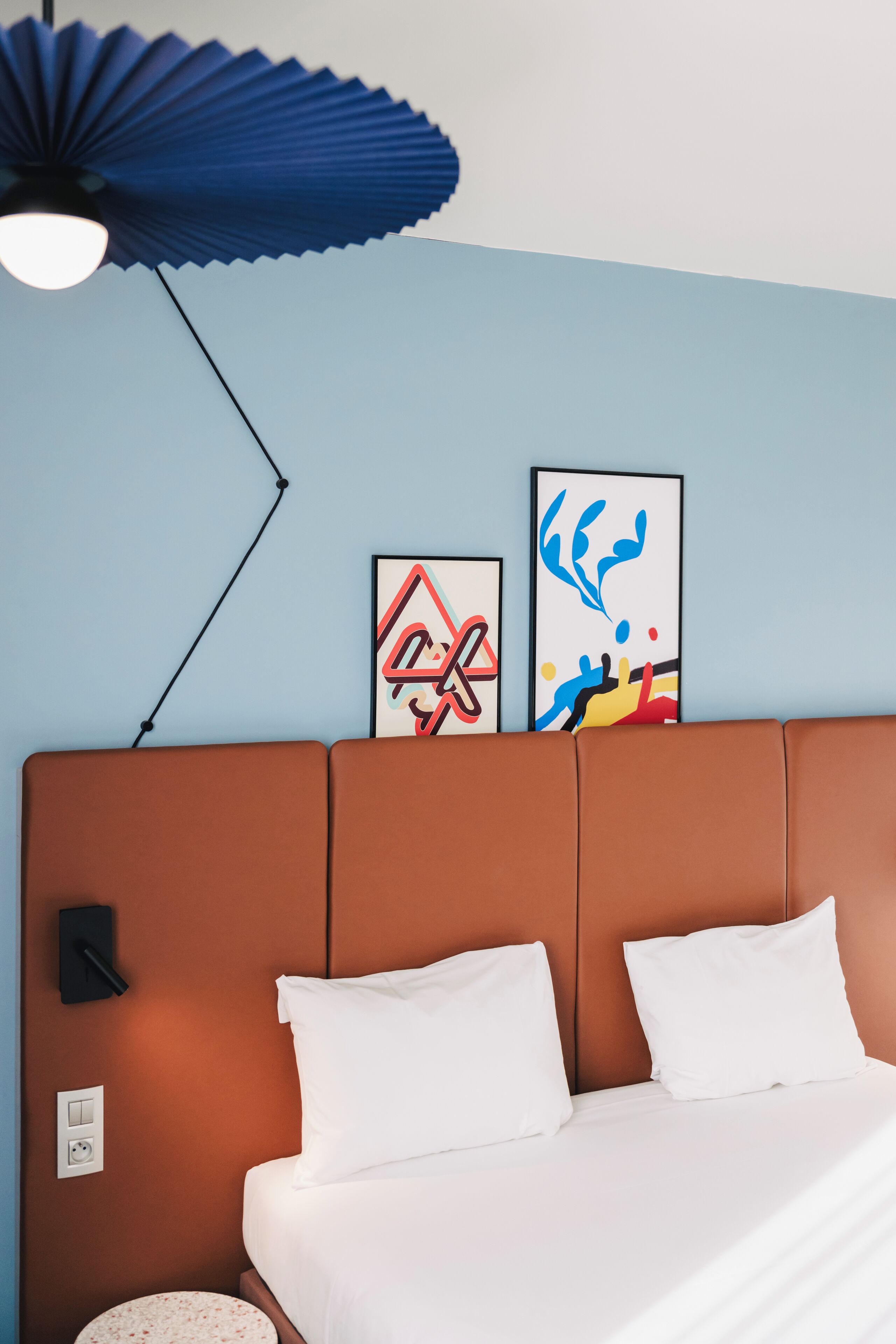 Une chambre d’hôtel avec une tête de lit marron, du linge de lit blanc et deux œuvres d’art abstraites accrochées au mur.