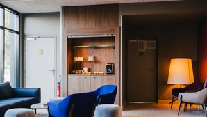 Um hall de hotel moderno com área de estar, kitchenette e uma luminária.