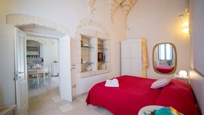 A bedroom with a red bedspread, a bedside table with a book, and an arched ceiling. - La Torre nel Borgo (Melendugno)
