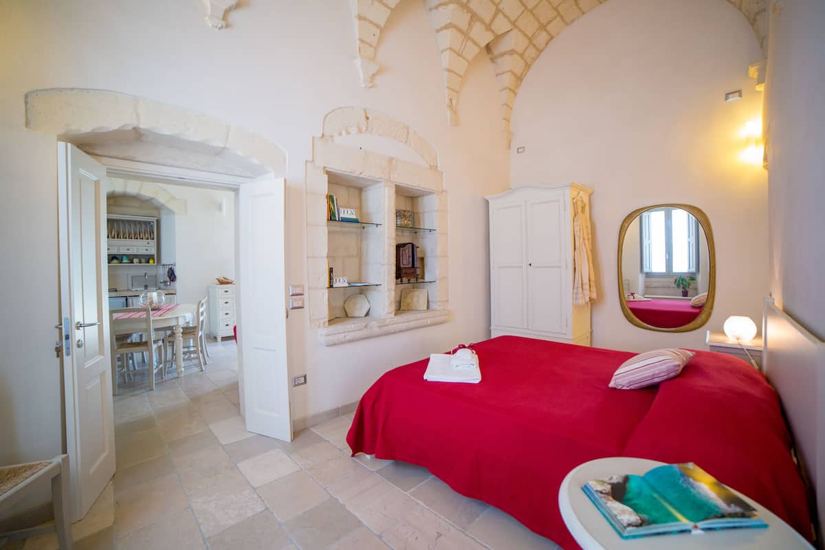 A bedroom with a red bedspread, a bedside table with a book, and an arched ceiling.