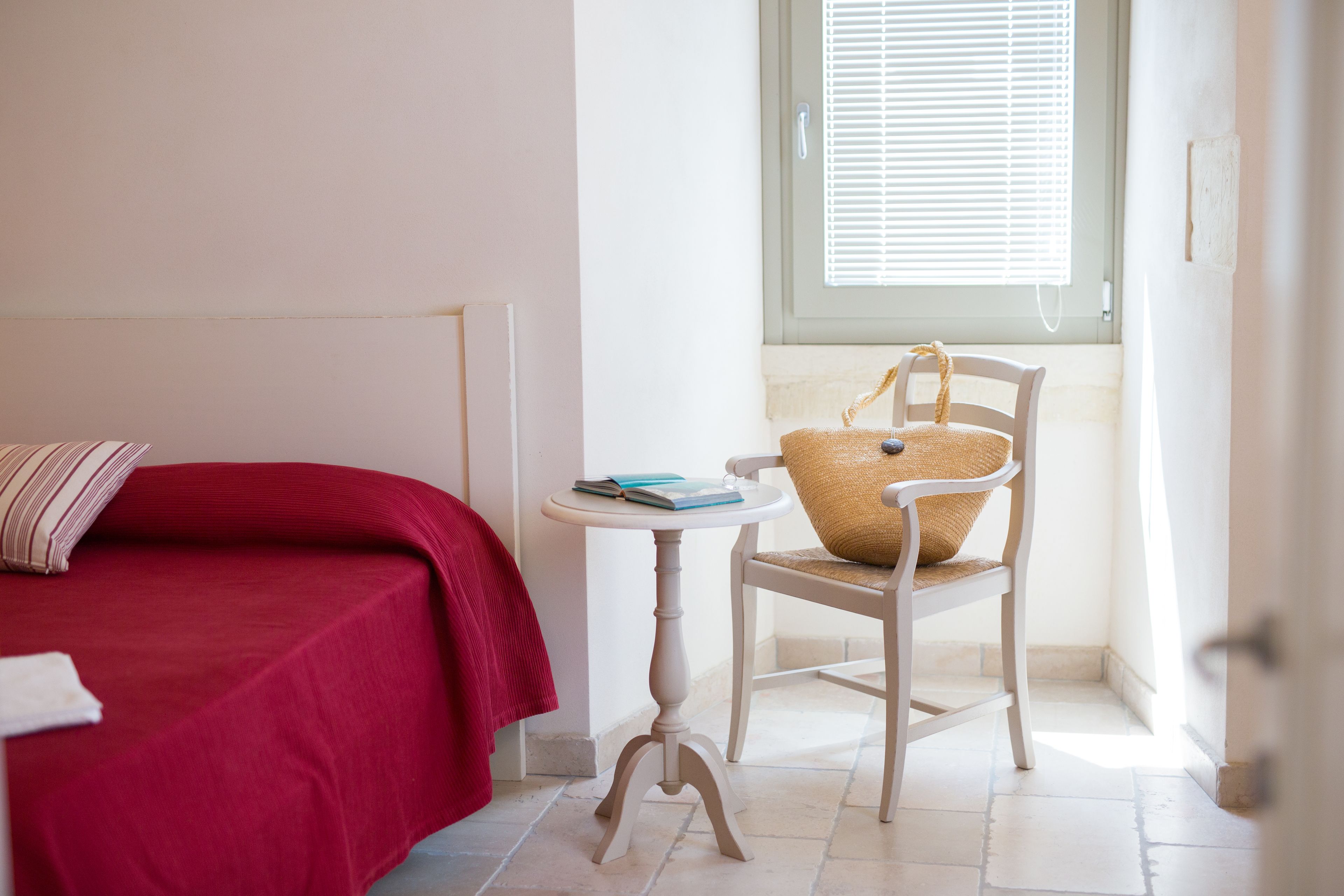 Un dormitorio con cama, una silla, una mesita y una ventana con persianas.