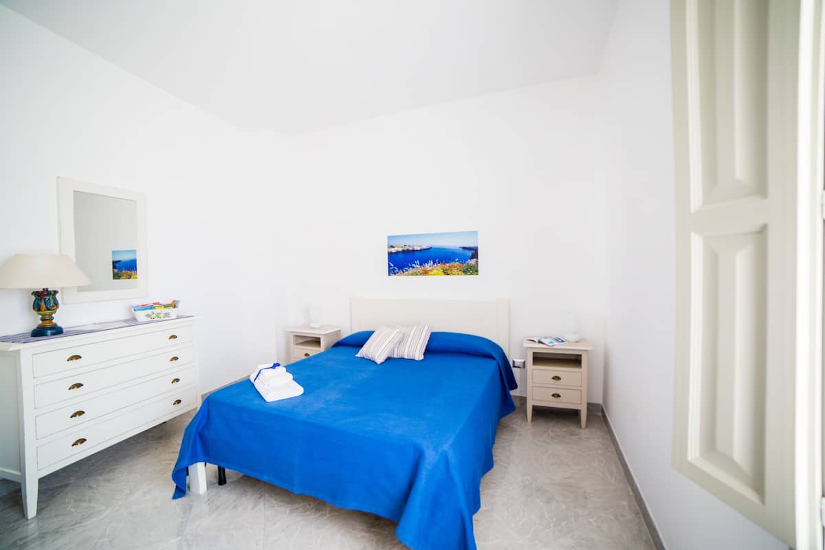 A bedroom with a bed, a dresser, a nightstand, a lamp, and a picture on the wall.
