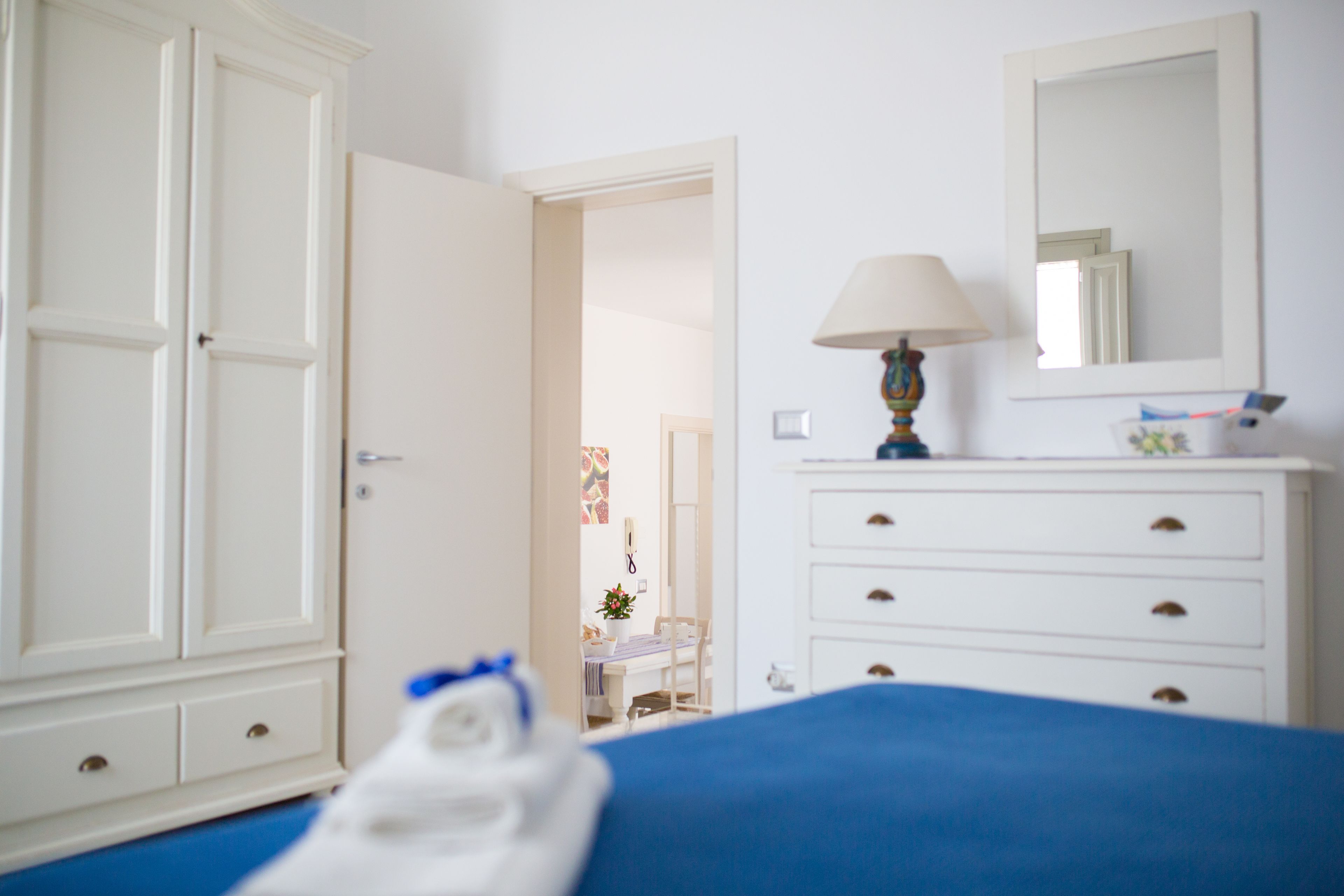Une chambre à coucher comprenant un lit, une commode, un miroir et une porte donnant sur une autre pièce.