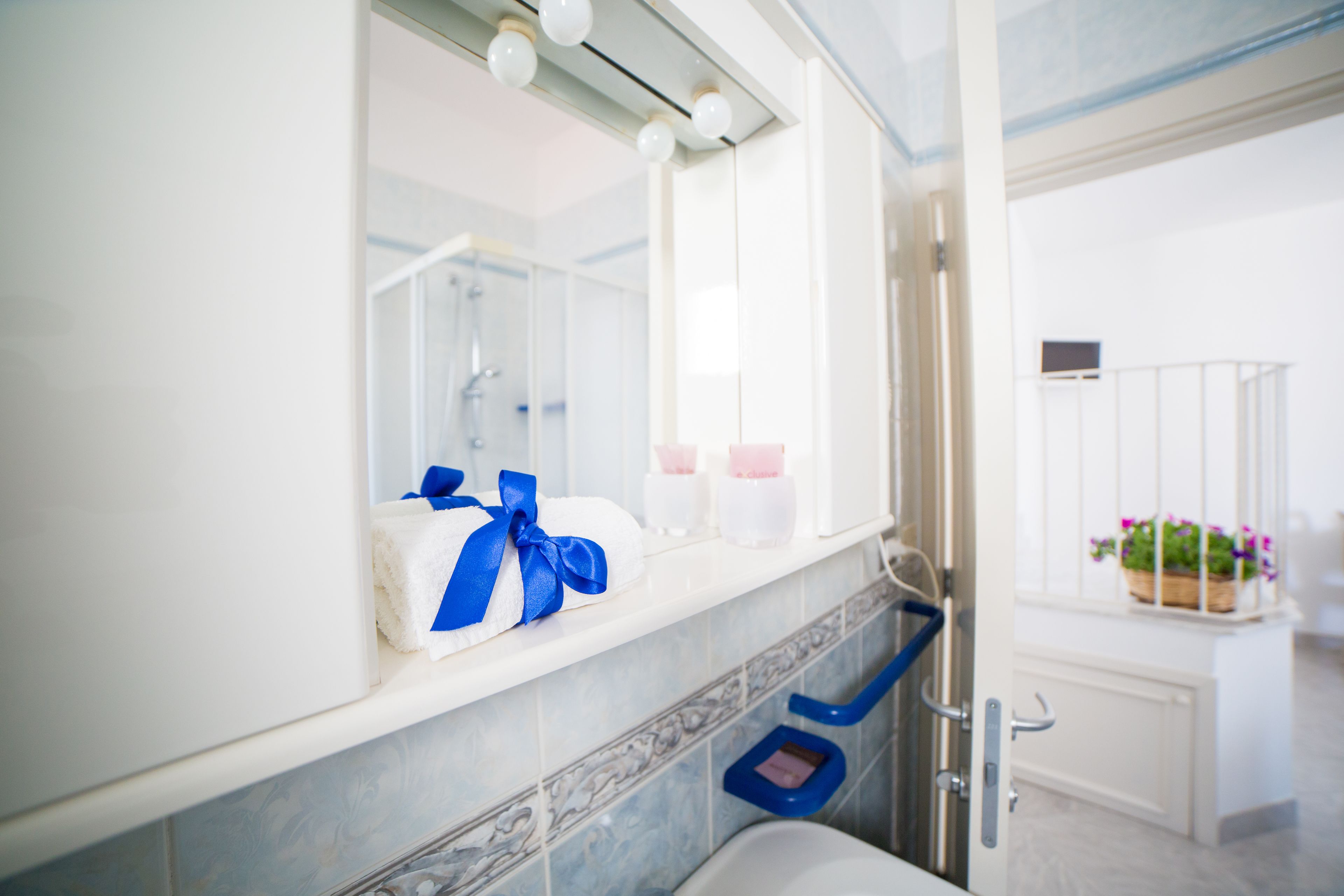 Een badkamer met een wit wastafel, een spiegel, een handdoek met een blauwe lint en een douchegedeelte.