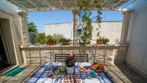 A table set for a meal with a blue and white striped tablecloth, potted plants, and a fruit bowl. - La Torre nel Borgo (Melendugno)
