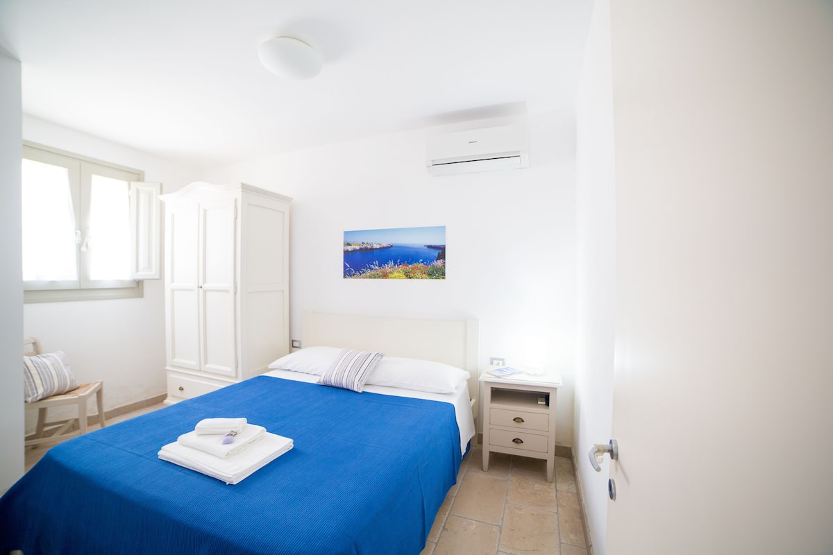 A bedroom with a bed, a nightstand, a window, and an air conditioning unit.
