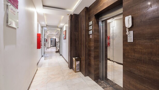 Un pasillo de hotel con piso de mármol, paneles de madera, un teléfono y una puerta de ascensor de vidrio.