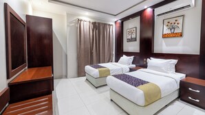 Habitación de hotel con dos camas, un escritorio de madera, un armario, una ventana con cortinas y un equipo de aire acondicionado.