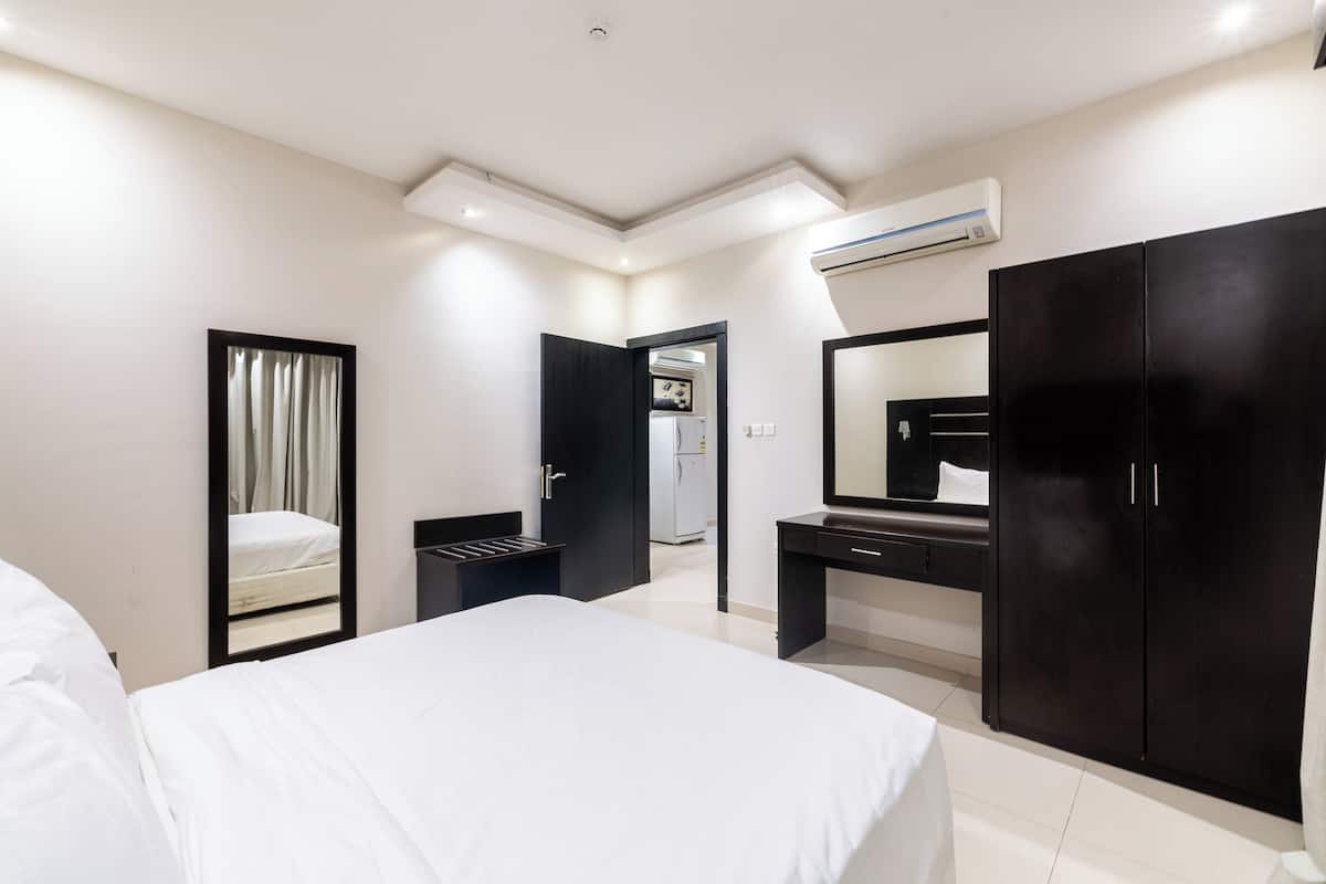 A modern hotel room with a bed, a desk, a wardrobe, and an air conditioning unit.