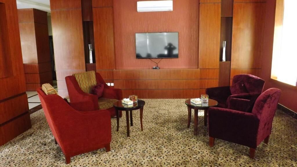 Une pièce avec un téléviseur fixé au mur, deux fauteuils, une petite table et un tapis à motifs.