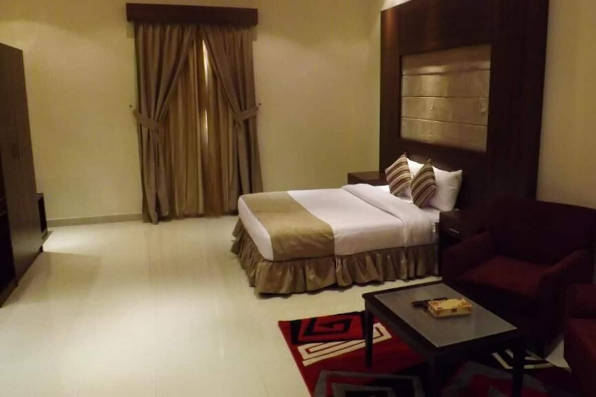 A hotel room with a bed, two chairs, a small table, a TV, and a painting on the wall.