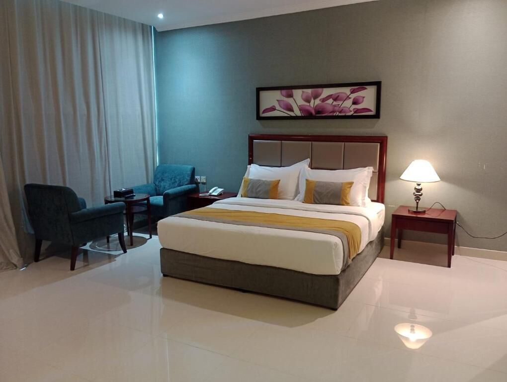 Quarto de hotel com cama, uma cadeira, mesa de cabeceira e abajur.