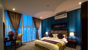 A hotel room with a large bed, a chair, a nightstand, and a window with curtains. - Taleen Al Hasa (Al-Hofuf)