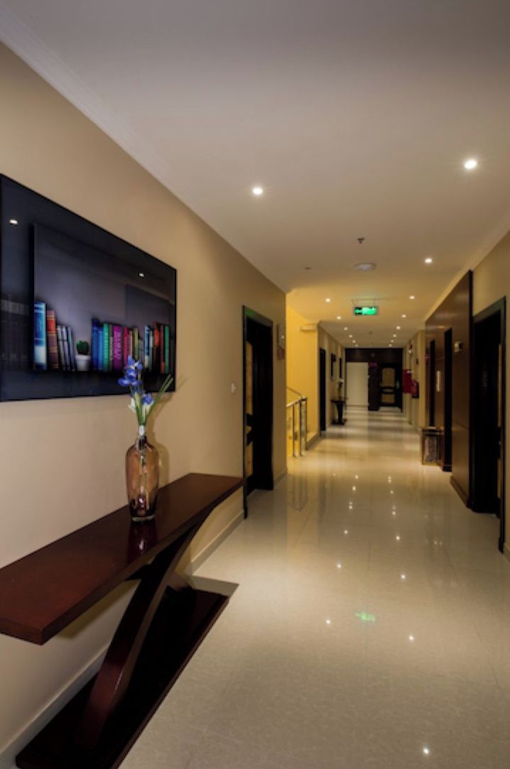 A hotel hallway with a long corridor, a reception desk, and a wall-mounted bookshelf.