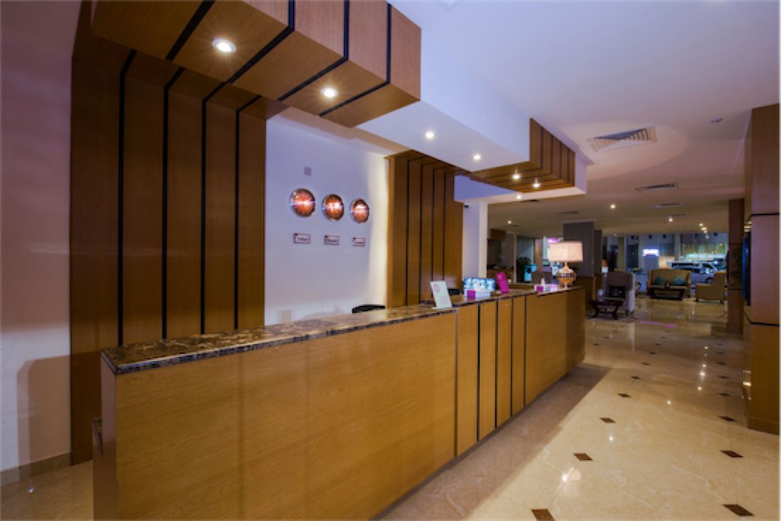 A reception area with a wooden reception desk, a marble floor, and a view into a lounge area with seating.