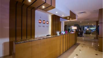 A reception area with a wooden reception desk, a marble floor, and a view into a lounge area with seating.