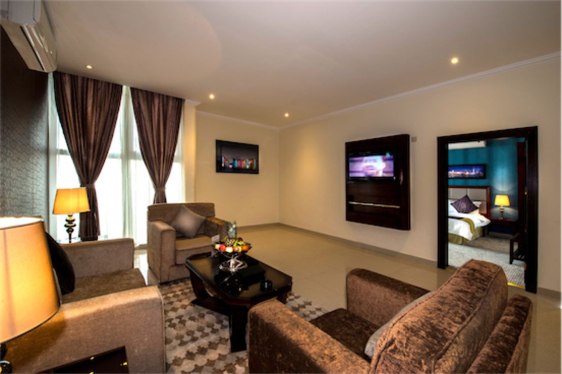 A hotel room with a sofa, armchair, and a television on the wall.