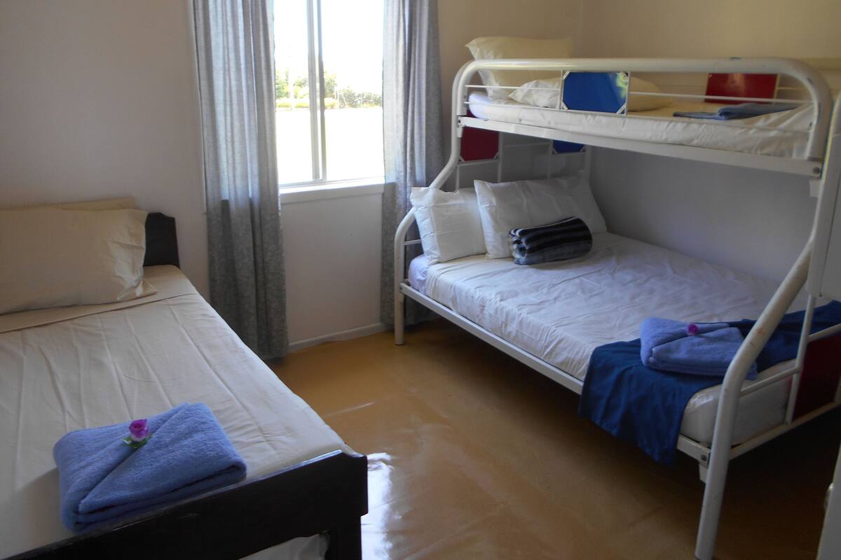 Une chambre avec un lit superposé, un lit simple et une fenêtre avec des rideaux.