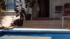 Piscina amb escales blaves que hi condueixen, envoltada de plantes en testos i una cadira.
