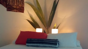 Un llit ben fet amb estovat blau i blanc, un coixí vermell i un coixí rayat. Hi ha dues làmpades de nit i una planta a la cantonada.