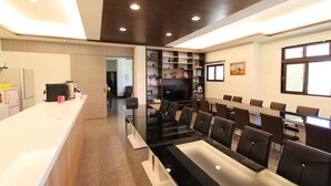 Una sala de reuniones moderna con una larga mesa, sillas, un televisor y una estantería.